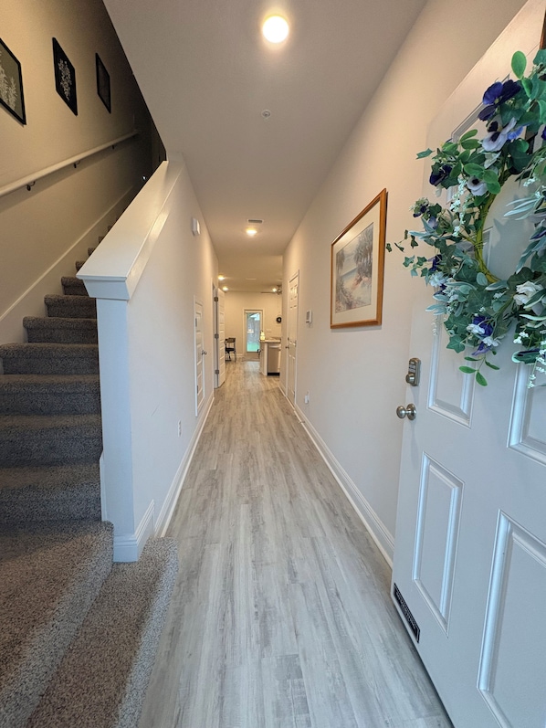 A hallway with carpeted stairs, a light-colored floor, and a door with a decorative plant.