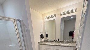 A bathroom with a glass shower enclosure, a vanity with a sink, a large mirror, and a lighted vanity area. - Fresh Townhome in Pensacola (Pensacola)