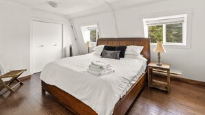 Een slaapkamer met een groot bed, een houten hoofdbord, een nachtkastje met een lamp en een raam dat voor natuurlijk licht zorgt.