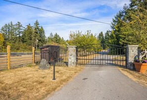 A gated entrance with a metal gate, a stone pillar, and a small structure to the left. - Amazing 2-bedroom cottage in Victoria, perfect for relaxing getaways. (Victoria)