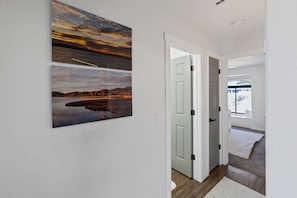 A hallway with two landscape paintings, a white door, and a view into a room with a window. - Lake Havasu Retreat w Private Pool & Spa, Lake Views + Boat Parking (Lake Havasu City)