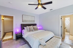 Ein Schlafzimmer mit einem Bett, einem Deckenventilator, einem Nachttisch, einer Wandleuchte und einer Tür zu einem anderen Raum.
