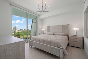 A modern bedroom with a large bed, bedside lamps, a view of the city, and a balcony. - Brand-New Furnished Luxury, Sophisticated Turnkey at a Premier Address (North Miami)