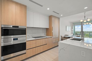 A modern kitchen with stainless steel appliances, wooden cabinets, and a large window offering a city view. - Brand-New Furnished Luxury, Sophisticated Turnkey at a Premier Address (North Miami)