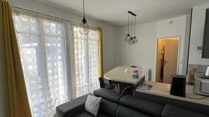 Een moderne woonkamer met een donker leren bank, een eethoek met een tafel en stoelen, en een keuken met een magnetron.