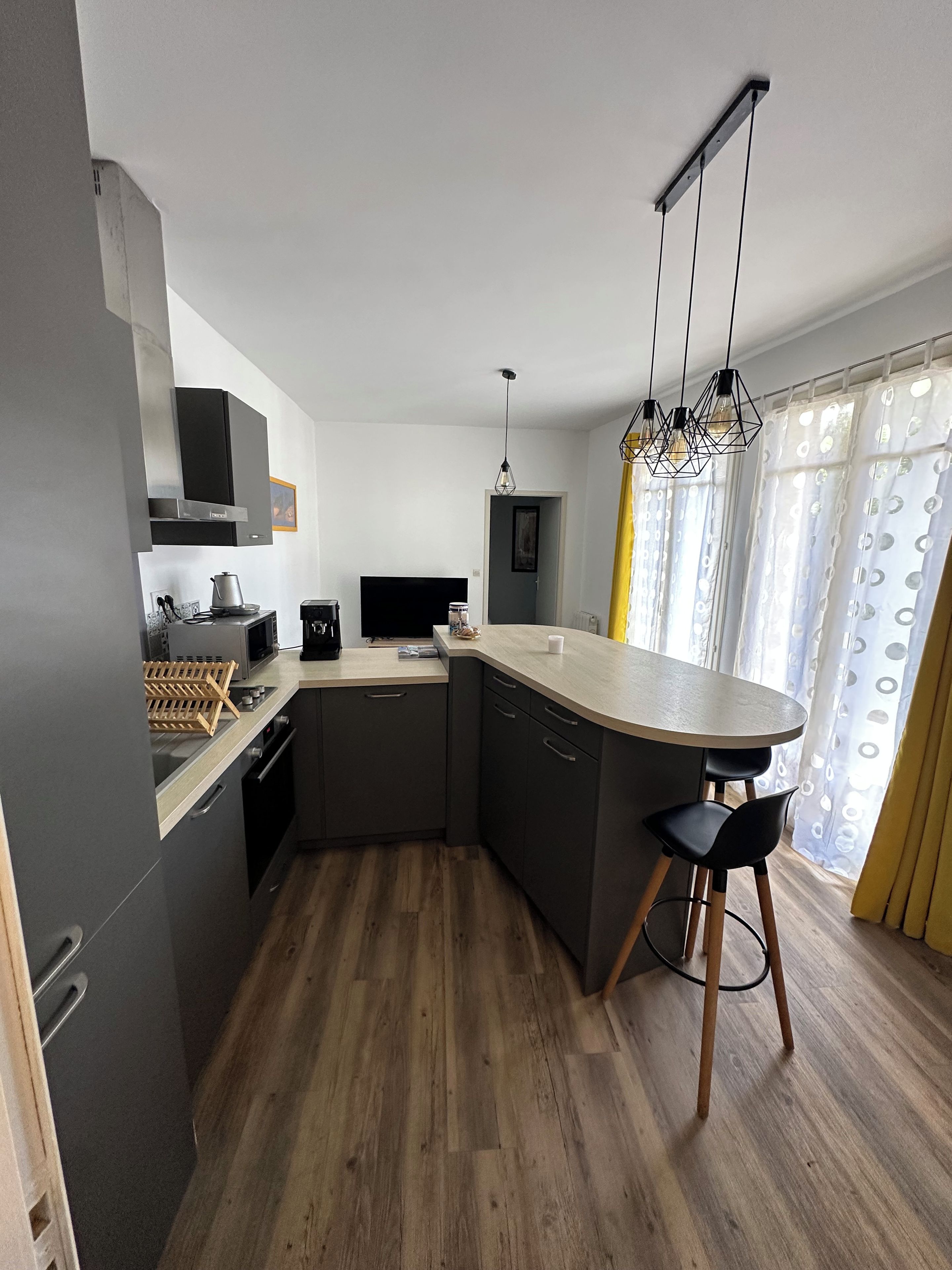 Een moderne keuken met een centraal eiland, donkere kastjes en een houten vloer.