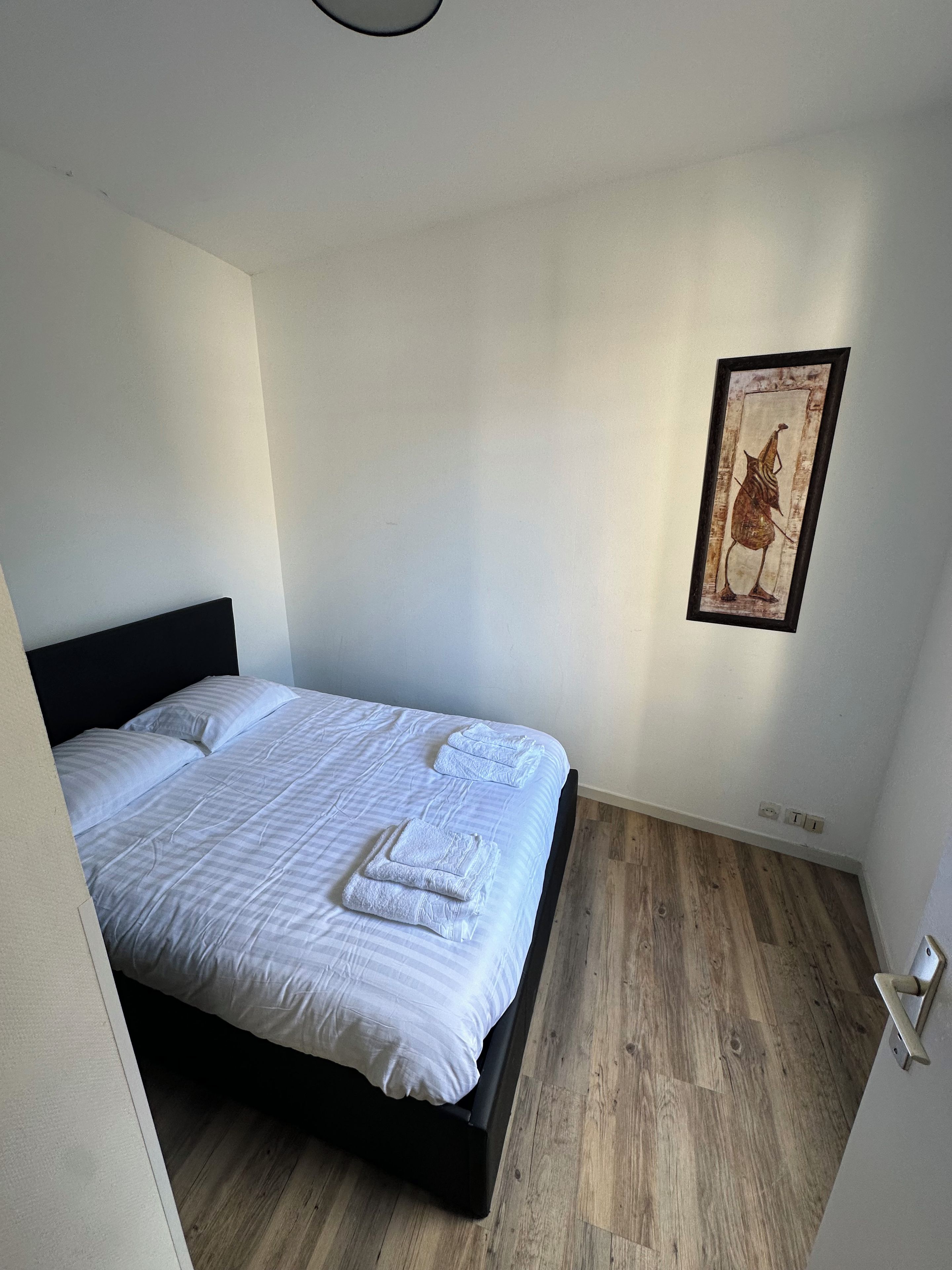 Un dormitorio con cama, almohadas, una obra de arte enmarcada en la pared y suelo de madera.