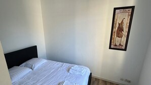 Een slaapkamer met een bed, kussens, een lijst met een kunstwerk en een houten vloer.