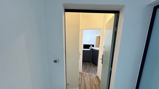 Een gang die uitkomt in een keuken met betegelde vloer en een zichtbare gootsteen.