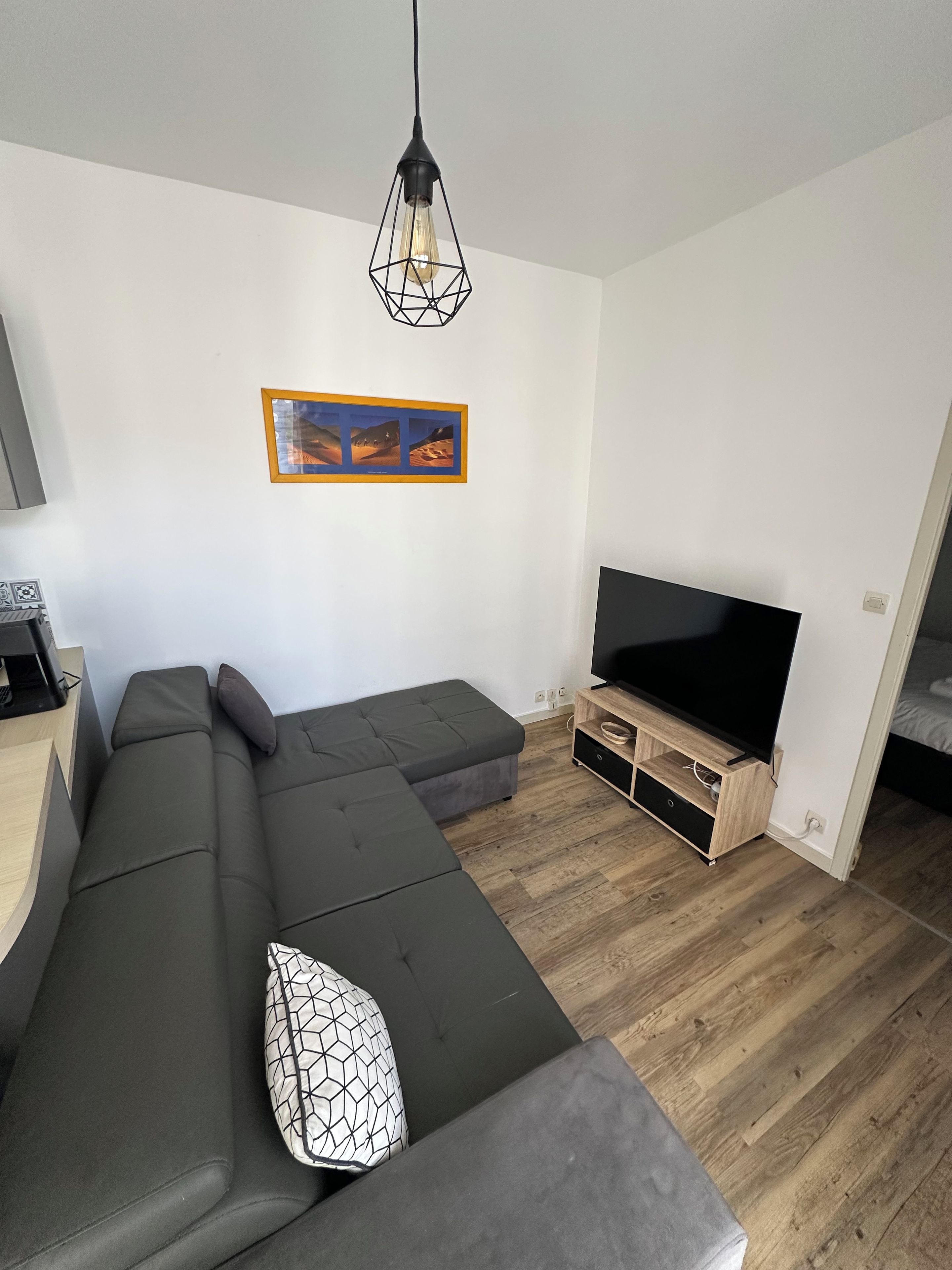 Een moderne woonkamer met een modulaire bank, een flatscreen televisie, een houten tv-meubel en een hanglamp.