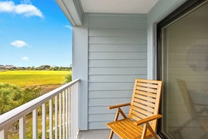 A wooden chair on a balcony with a view of a green field and distant buildings. - Elevated Seaside Sanctuary With Beach Gear (Hilton Head Island)