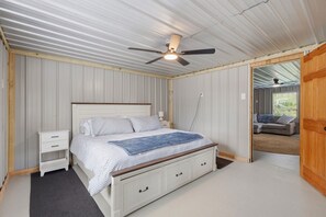 Ein Schlafzimmer mit Bett, Nachttischen, Deckenventilator und Blick in einen angrenzenden Raum.