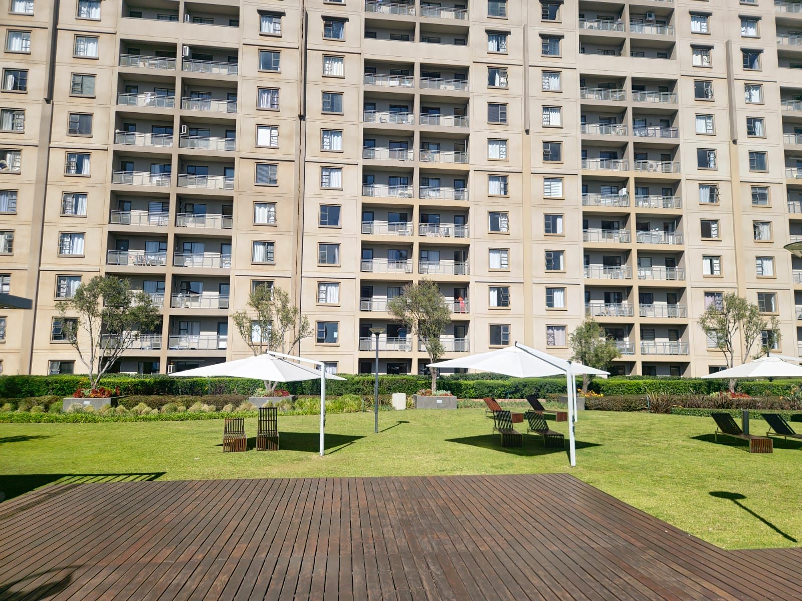 Un edificio residencial de varios pisos con balcones, un patio con césped y mobiliario exterior, y una terraza de madera.