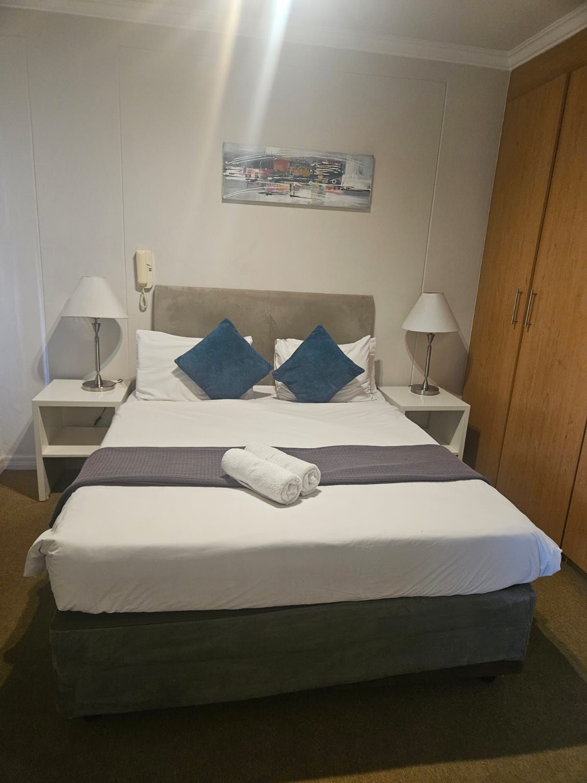 Une chambre d’hôtel avec un lit, deux tables de chevet, un téléphone, un tableau et une armoire.
