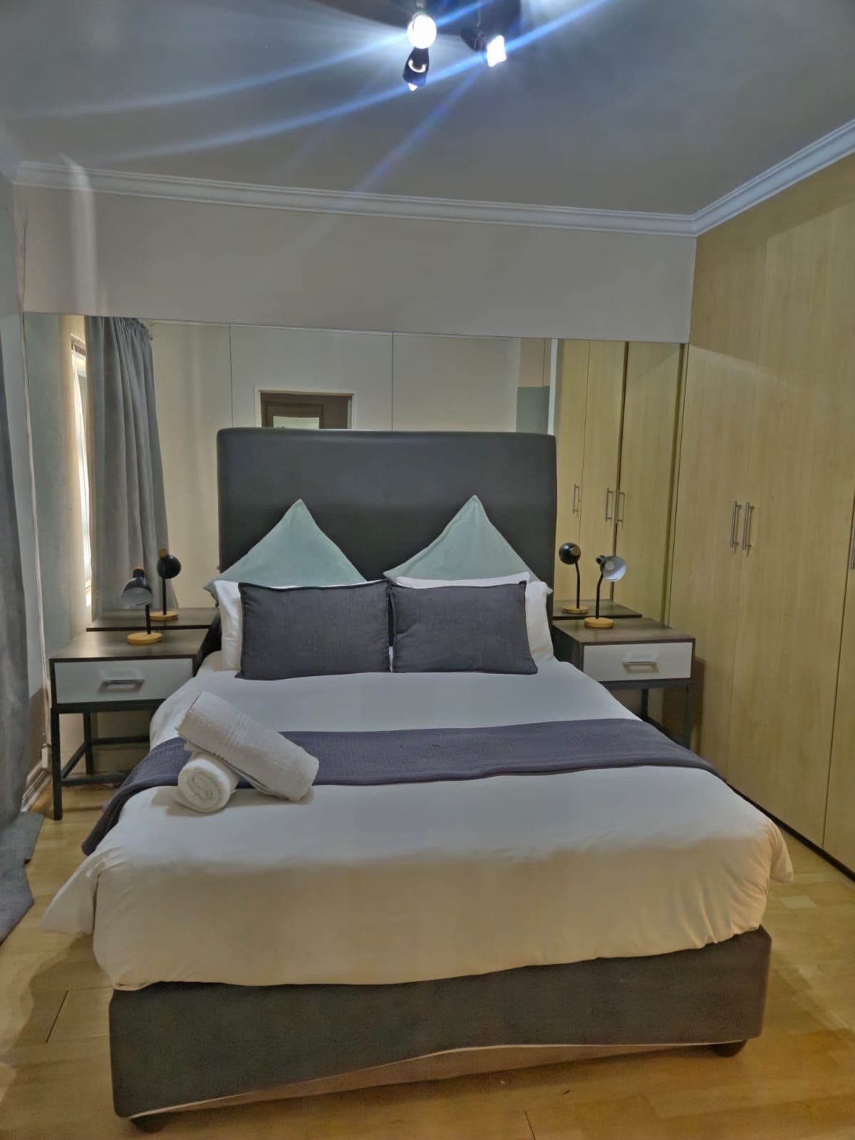 Una cama bien hecha con almohadas y una colcha, una mesita de noche con una lámpara y un armario en una habitación de hotel.
