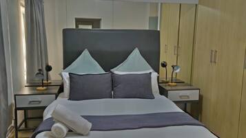 Una cama bien hecha con almohadas y una colcha, una mesita de noche con una lámpara y un armario en una habitación de hotel.