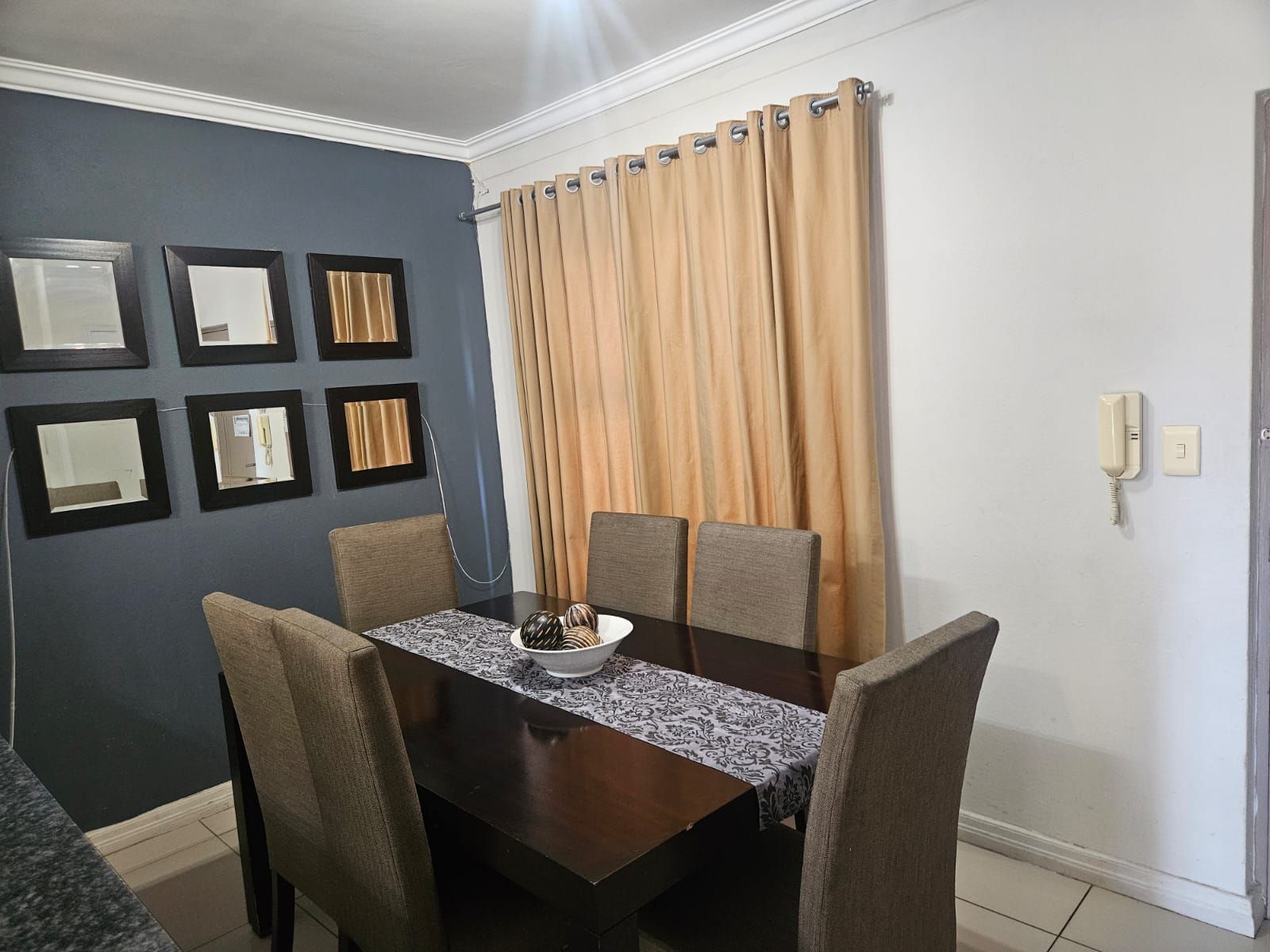 A dining area with a dark wooden table, six chairs, and a bowl of snacks.