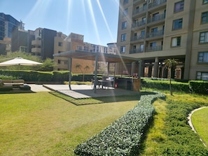 A courtyard with a covered seating area, a pathway, and well-maintained hedges. - Sandton Westpoint Luxury Apartments -172 (Sandton)