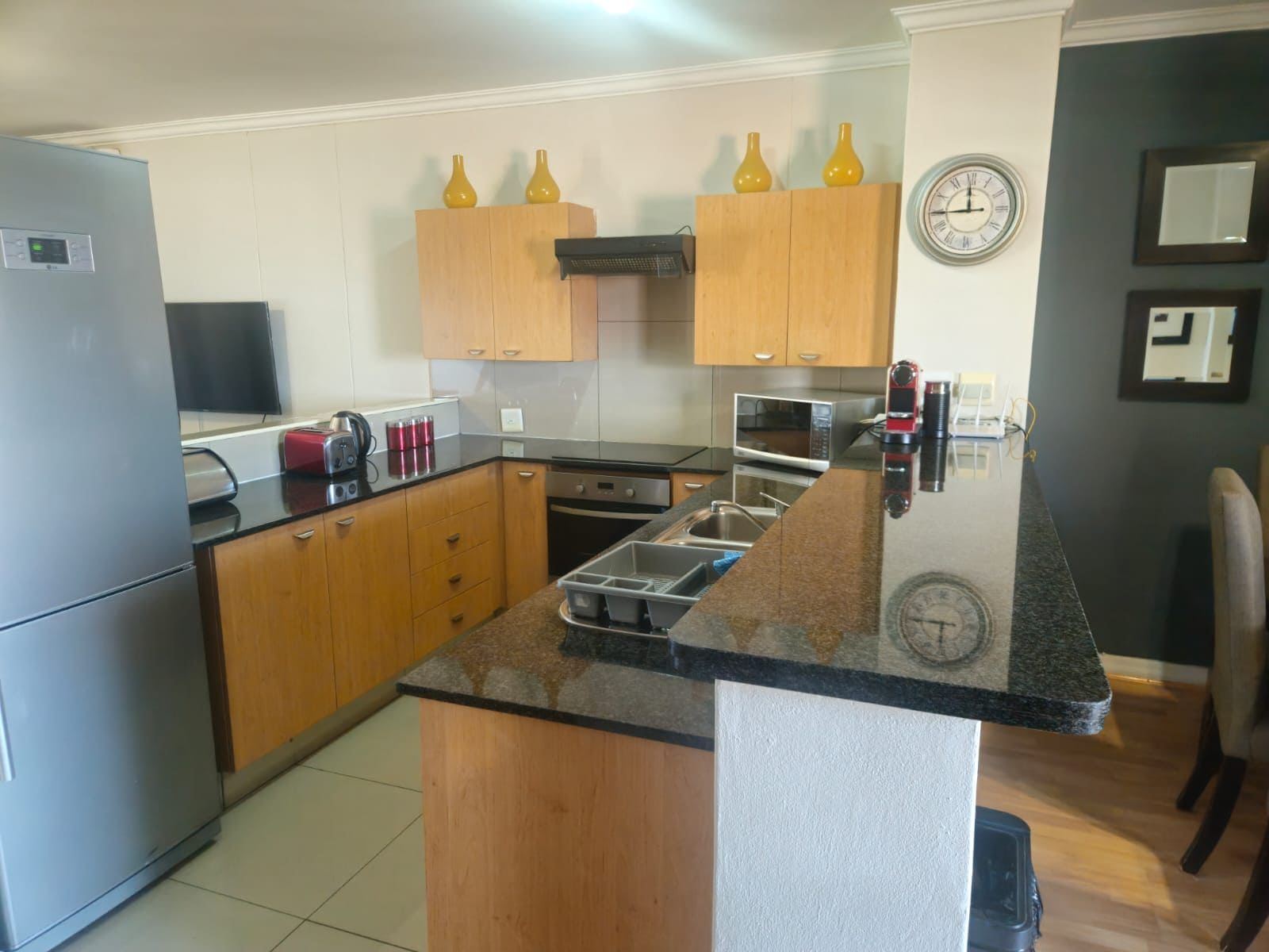 Una cocina con armarios de madera, encimera de granito, microondas, tostadora y un reloj en la pared.