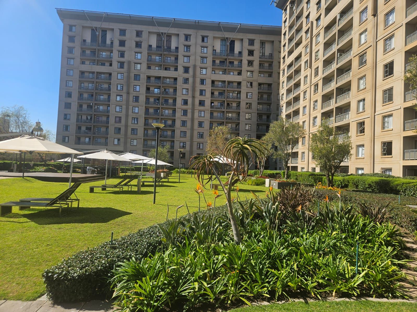 Un edificio residencial de gran altura con varios balcones, un césped bien cuidado y zonas de estar al aire libre.