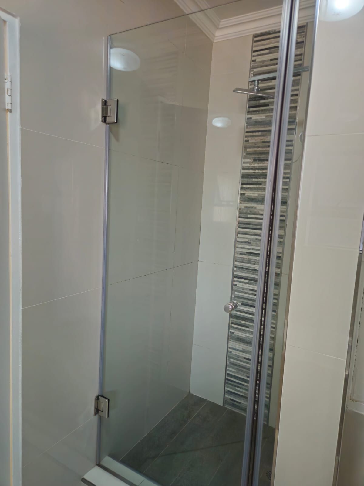 Cabina de ducha con paredes de vidrio, piso de azulejos y ducha metálica.