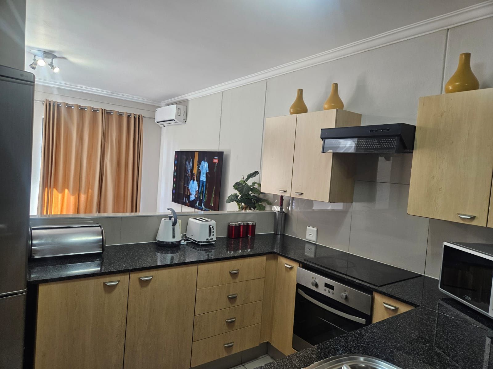 Una cocina moderna con armarios de madera, encimera negra, horno empotrado y televisor montado en la pared.