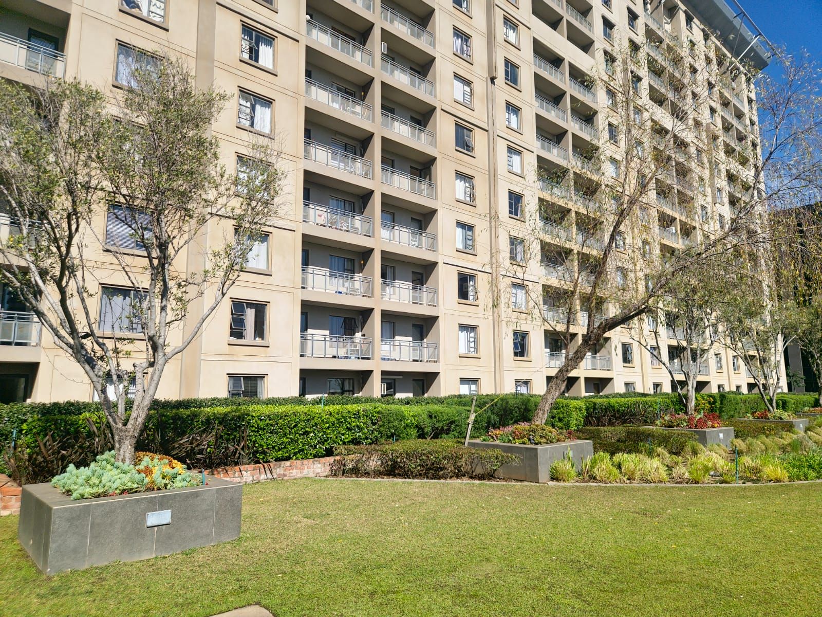 Un edificio residencial de varios pisos con balcones, rodeado de céspedes y árboles bien cuidados.