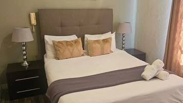 A hotel room with a large bed, two bedside tables, a framed picture on the wall, and a telephone on the left table.