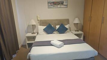 Una habitación de hotel con una cama, dos mesitas de noche, un armario y un cuadro en la pared.