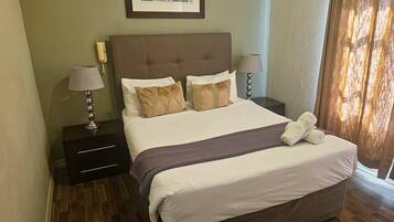 Habitación de hotel con cama, dos mesitas de noche, lámpara, un cuadro en la pared y ventana con cortinas.