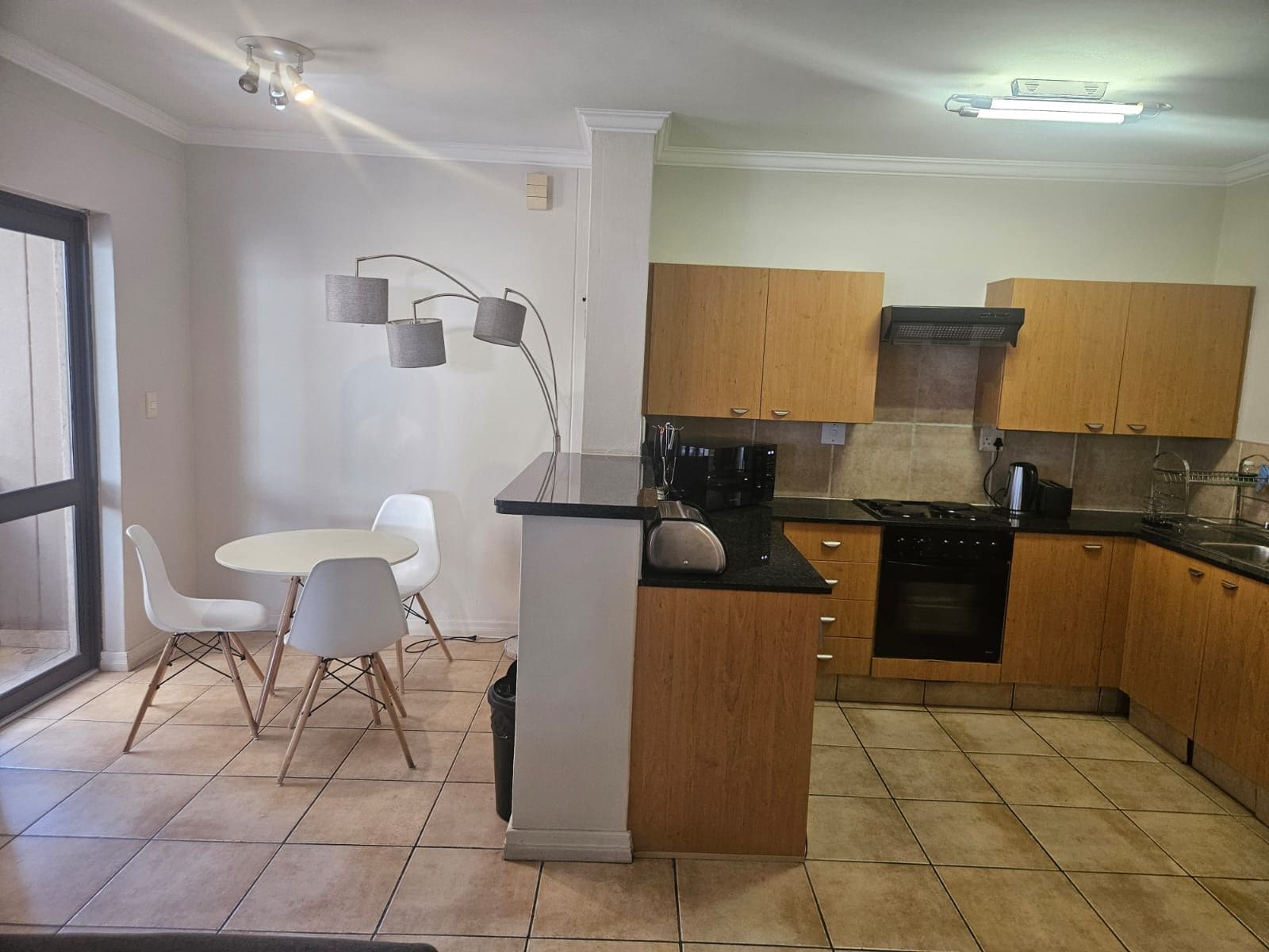 Een compacte keuken met een eethoek, met een centraal kookeiland, houten kastjes en een moderne lamp.