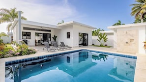Ein modernes Haus mit Schwimmbad, Sitzgelegenheiten im Freien und tropischen Pflanzen.