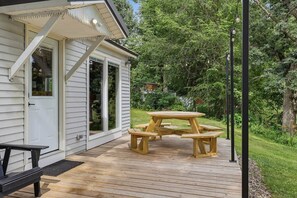 Un terrazzo in legno con tavolo da picnic e panche, immerso nel verde.
