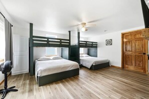 Una stanza con due letti a castello, una ventola a soffitto, una porta in legno e un ventilatore a terra.
