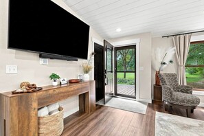 Ein modernes Wohnzimmer mit Flachbildfernseher, Holztischchen, Korbwäsche und einem gemusterten Sessel.