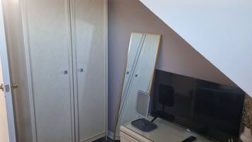 A room with a desk, a mirror, a wardrobe, and a television.
