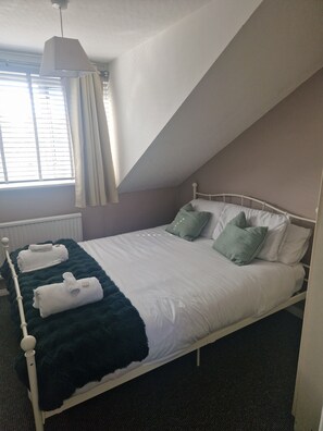 A single-bed room with a sloped ceiling, a window with blinds, a white radiator, and a dark green throw blanket. - Quiet and peaceful living space with off-road parking. (London)