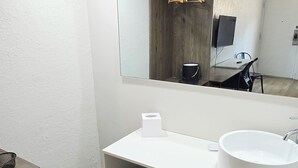 Ein modernes Badezimmer mit einem weißen Waschbecken, einem Spiegel und einer Holz-Waschkommode.