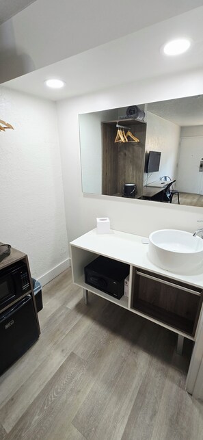 A modern bathroom with a white sink, a mirror, and a wooden vanity. - Cozy 2-Queen Room, Pool, Near Disney & Attractions. (Kissimmee)