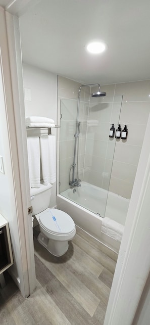 A modern bathroom with a glass-enclosed shower, a white toilet, and a glass-enclosed bathtub. - Cozy 2-Queen Room, Pool, Near Disney & Attractions. (Kissimmee)