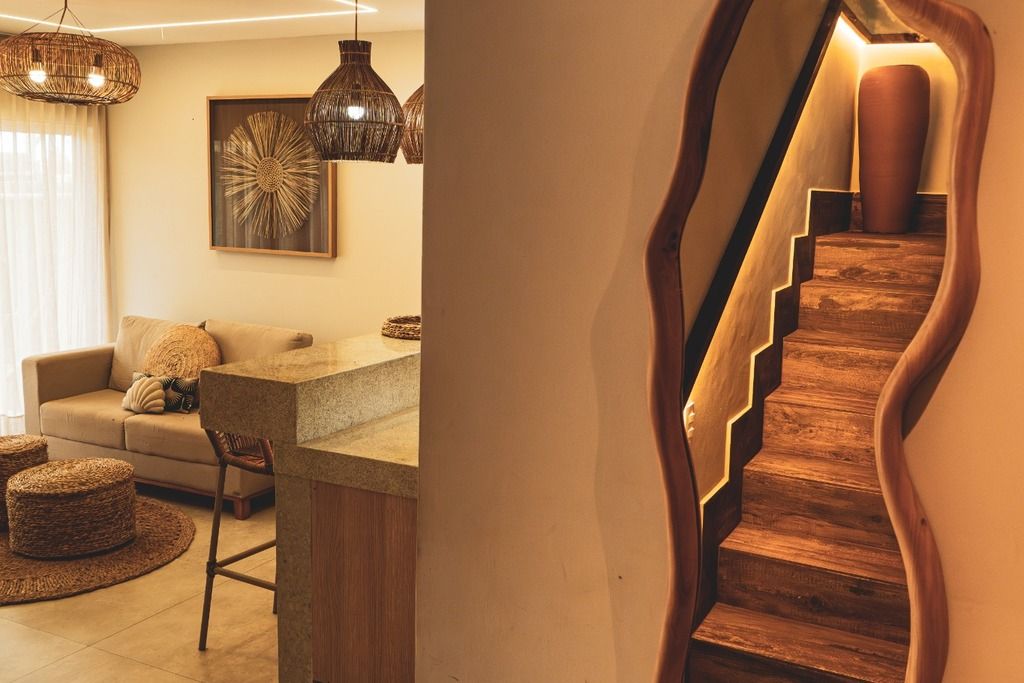 A modern living room with a sofa, a coffee table, and wicker ottomans. There is a staircase with wooden steps and a unique wall design.