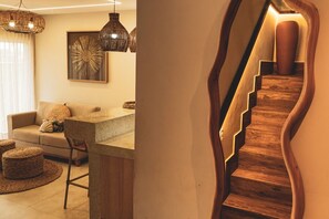A modern living room with a sofa, a coffee table, and wicker ottomans. There is a staircase with wooden steps and a unique wall design.