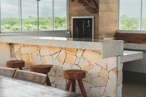 A kitchen with a stone backsplash, wooden stools, and a view of greenery outside.