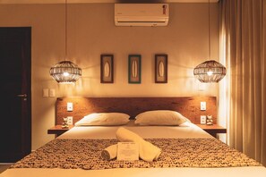 A hotel room with a bed, two bedside tables, a wall-mounted air conditioner, and two hanging lamps.