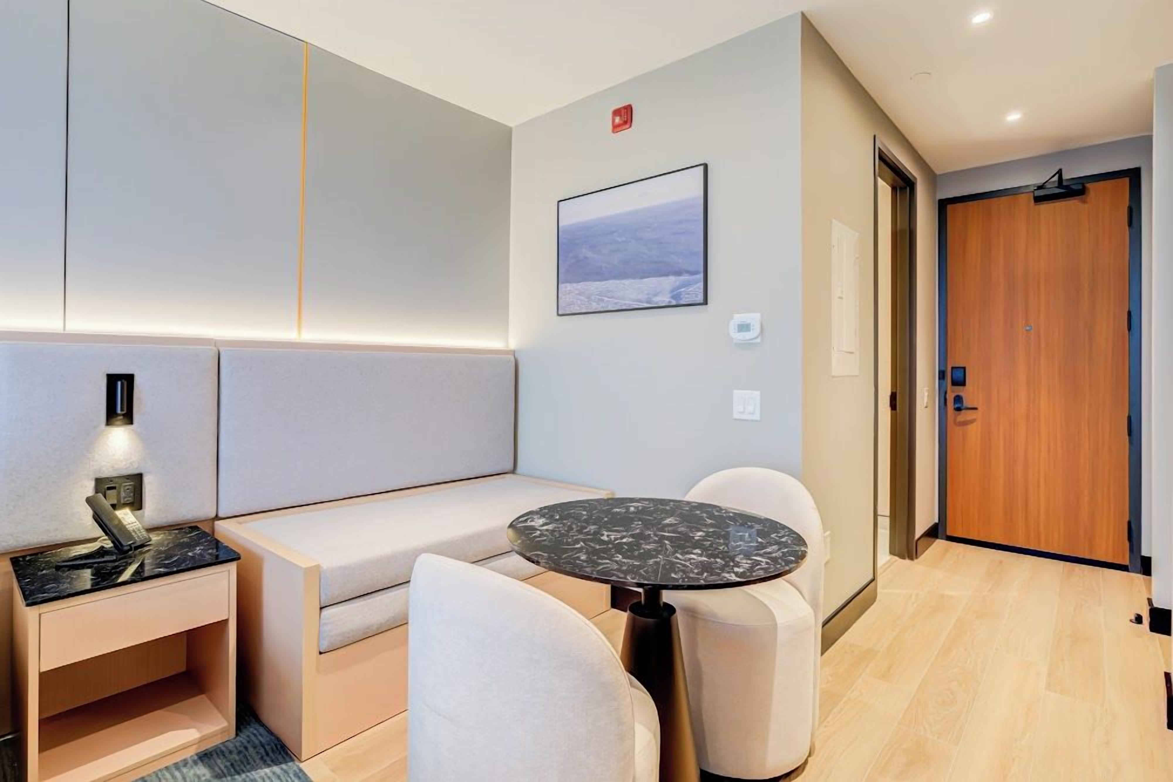 Una habitación de hotel moderna con un sofá, una pequeña mesa redonda y una mesita de noche con lámpara.