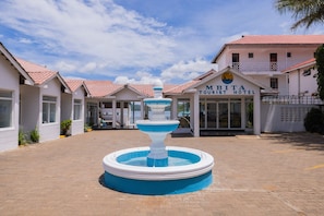 A tourist hotel with a central fountain, multiple buildings with red-tiled roofs, and a clear sky.