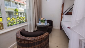 A balcony with wicker furniture, a small table with water bottles and a potted plant, and a bed with white bedding. - Mbita Tourist Hotel (Mbita)