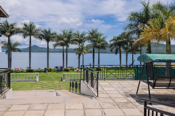 A terrace with a view of a lake, palm trees, and a distant mountain range.