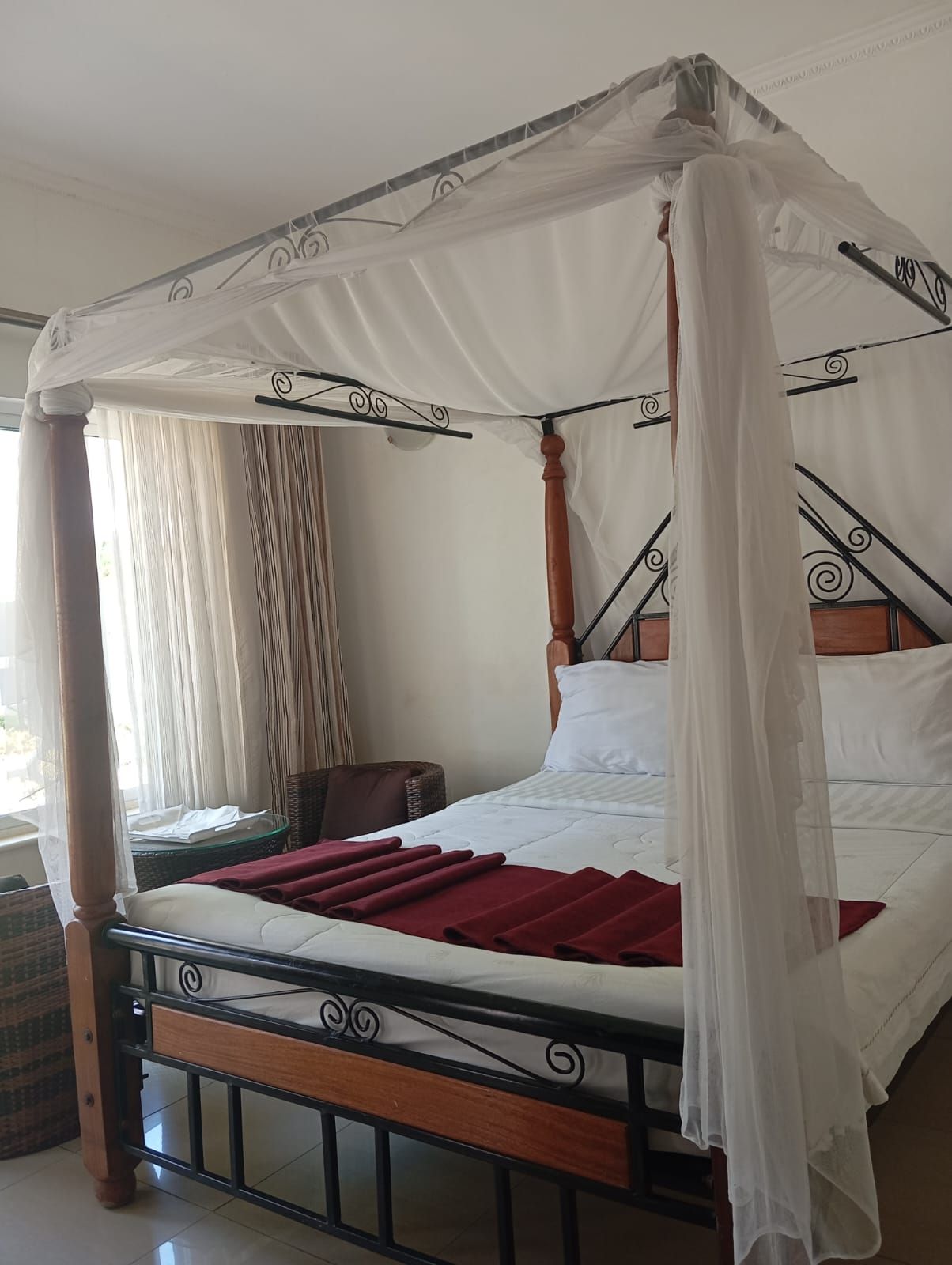 Uma cama com dossel e colunas de madeira, com roupa de cama branca.