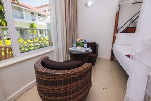 A balcony with wicker furniture, a small table with water bottles and a vase of flowers, and a bed with white bedding.